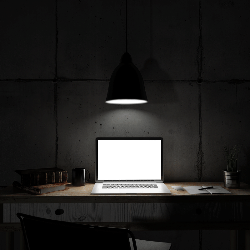 Laptop on table in dark room with light shining above